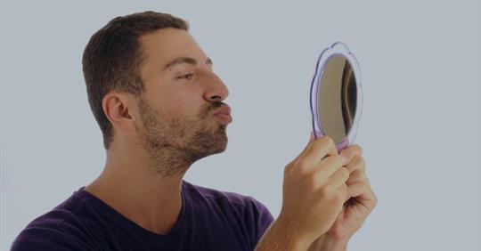 A man staring at his reflection in the mirror, clearly in love with his appearance